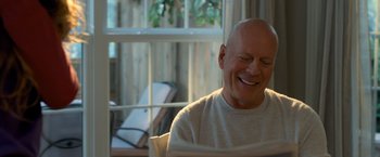 Movie still from “Death Wish” (2018), directed by Eli Roth – An older bald man sitting in a chair smiling; Close Up shot, Over the shoulder angle