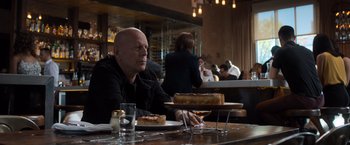 Movie still from “Death Wish” (2018), directed by Eli Roth – A man sitting at a table with a plate of cake; Medium shot, Over the shoulder angle