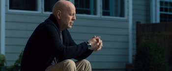 Movie still from “Death Wish” (2018), directed by Eli Roth – A bald man sitting on the ground with his hands clasped together; Medium shot, Low angle