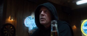 Movie still from “Death Wish” (2018), directed by Eli Roth – A man in a hooded jacket is sitting at a table with a bottle of beer in front of him; Close Up shot, Low angle
