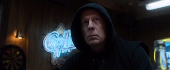 Movie still from “Death Wish” (2018), directed by Eli Roth – A man wearing a black hoodie with a neon sign behind him; Close Up shot, Low angle