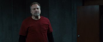 Movie still from “Death Wish” (2018), directed by Eli Roth – A man in a red shirt is standing in front of a black wall; Medium shot, Low angle