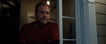 Movie still from “Death Wish” (2018), directed by Eli Roth – A man in a red shirt looking out of a window; Close Up shot, Low angle