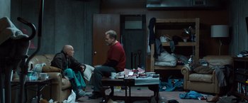 Movie still from “Death Wish” (2018), directed by Eli Roth – Two people sitting on a table in a room; Wide shot, High angle