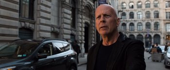 Movie still from “Death Wish” (2018), directed by Eli Roth – A man standing on the side of the street in front of a building; Close Up shot, Low angle