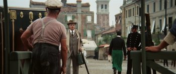 Movie still from “Death in Venice” (1971), directed by Luchino Visconti – A man in a suit and hat is walking down the street; Wide shot, Over the shoulder angle