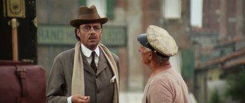 Movie still from “Death in Venice” (1971), directed by Luchino Visconti – A man wearing a hat and a tie talking to another man; Medium shot, Over the shoulder angle