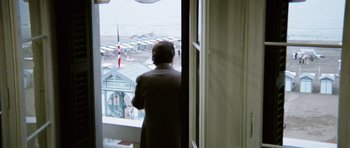 Movie still from “Death in Venice” (1971), directed by Luchino Visconti – A man standing in front of an open window looking out at the ocean; Wide shot, Over the shoulder angle