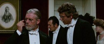 Movie still from “Death in Venice” (1971), directed by Luchino Visconti – A group of men standing next to each other wearing tuxedos; Close Up shot, Over the shoulder angle