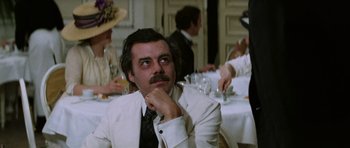 Movie still from “Death in Venice” (1971), directed by Luchino Visconti – A man sitting at a dinner table with his hand on his chin; Medium shot, Over the shoulder angle