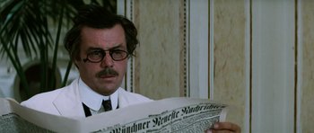 Movie still from “Death in Venice” (1971), directed by Luchino Visconti – A man in a white shirt and tie reading a newspaper; Close Up shot, Over the shoulder angle