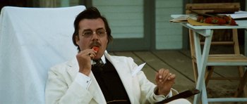 Movie still from “Death in Venice” (1971), directed by Luchino Visconti – A man in a white suit is eating a piece of paper; Medium shot, Low angle