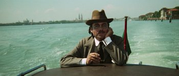 Movie still from “Death in Venice” (1971), directed by Luchino Visconti – A man sitting at a table in front of a body of water; Medium shot, Low angle