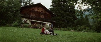 Movie still from “Death in Venice” (1971), directed by Luchino Visconti – A man and a woman sitting in the grass near a house; Wide shot, High angle