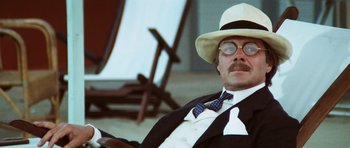 Movie still from “Death in Venice” (1971), directed by Luchino Visconti – A man in a suit and hat sitting in front of a chair; Close Up shot, Low angle