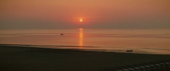 Movie still from “Death in Venice” (1971), directed by Luchino Visconti – The sun is setting over the ocean with a boat in the distance; Extreme Wide shot, High angle
