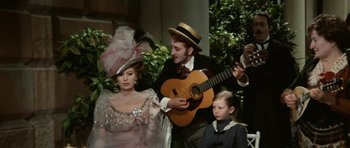 Movie still from “Death in Venice” (1971), directed by Luchino Visconti – A man playing a guitar next to a woman and a child; Medium shot, Low angle