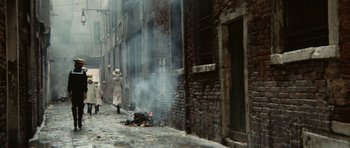 Movie still from “Death in Venice” (1971), directed by Luchino Visconti – An old woman walking down the street near a fire; Wide shot, High angle