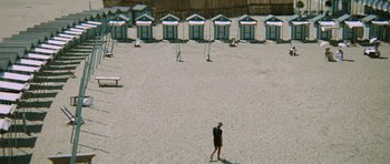 Movie still from “Death in Venice” (1971), directed by Luchino Visconti – A man standing on a beach near some beach huts; Extreme Wide shot, High angle