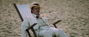 Movie still from “Death in Venice” (1971), directed by Luchino Visconti – A man in a white suit sitting in a chair on the beach; Wide shot, High angle