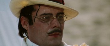 Movie still from “Death in Venice” (1971), directed by Luchino Visconti – A person wearing glasses and a hat; Close Up shot, Low angle