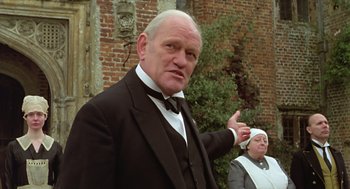 Movie still from “Death on the Nile” (1978), directed by John Guillermin – An older man in a suit and bow tie standing in front of an older woman; Medium shot, Low angle