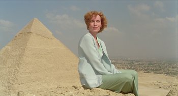 Movie still from “Death on the Nile” (1978), directed by John Guillermin – A woman sitting on top of a sand hill; Medium shot, Low angle