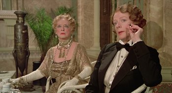 Movie still from “Death on the Nile” (1978), directed by John Guillermin – Two women in formal wear sitting next to each other; Medium shot, Low angle