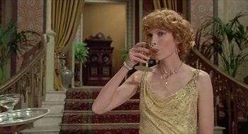 Movie still from “Death on the Nile” (1978), directed by John Guillermin – A woman in a gold dress drinking a glass of wine; Medium shot, Low angle