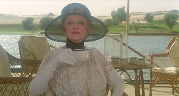 Movie still from “Death on the Nile” (1978), directed by John Guillermin – An older woman wearing a hat and holding a cup; Medium shot, Over the shoulder angle