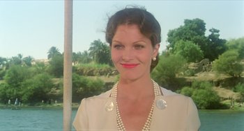 Movie still from “Death on the Nile” (1978), directed by John Guillermin – A woman wearing a white jacket and a pearl necklace; Close Up shot, Low angle