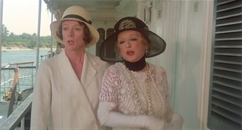 Movie still from “Death on the Nile” (1978), directed by John Guillermin – Two women dressed in white and wearing hats; Close Up shot, Over the shoulder angle