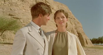 Movie still from “Death on the Nile” (1978), directed by John Guillermin – A man and a woman standing next to each other in front of a rock wall; Medium shot, Low angle