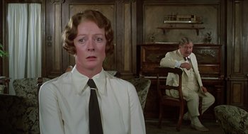 Movie still from “Death on the Nile” (1978), directed by John Guillermin – A woman wearing a white dress shirt and a black tie in front of a man in a white suit; Medium shot, Over the shoulder angle