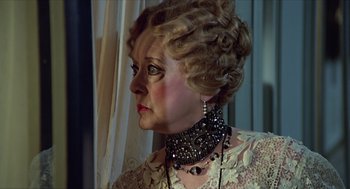 Movie still from “Death on the Nile” (1978), directed by John Guillermin – An older woman wearing a dress and a necklace; Close Up shot, Over the shoulder angle