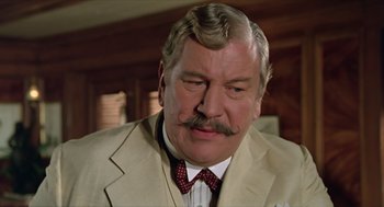 Movie still from “Death on the Nile” (1978), directed by John Guillermin – An older man in a suit and a tie; Close Up shot, Low angle
