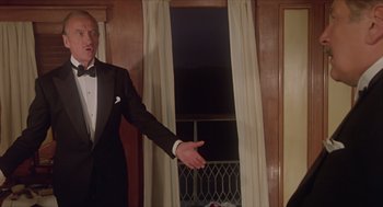 Movie still from “Death on the Nile” (1978), directed by John Guillermin – A man in a tuxedo standing in front of a window; Medium shot, Low angle