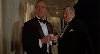 Movie still from “Death on the Nile” (1978), directed by John Guillermin – Two men in tuxedos standing next to each other; Medium shot, Over the shoulder angle