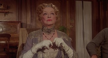 Movie still from “Death on the Nile” (1978), directed by John Guillermin – An older woman wearing gloves and a necklace; Close Up shot, Over the shoulder angle