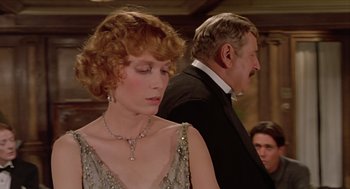 Movie still from “Death on the Nile” (1978), directed by John Guillermin – A man and a woman standing next to each other in front of a crowd; Close Up shot, Over the shoulder angle