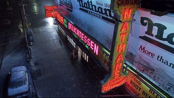 Movie still from “Death to Smoochy” (2002), directed by Danny DeVito – Neon signs lit up on the side of a building in the rain; Extreme Wide shot, Overhead angle