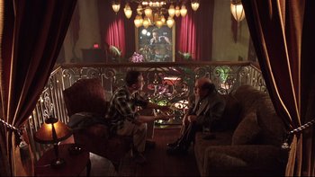 Movie still from “Death to Smoochy” (2002), directed by Danny DeVito – Two men sitting on a couch in front of a railing; Wide shot, High angle
