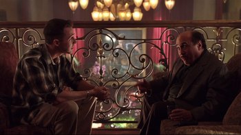 Movie still from “Death to Smoochy” (2002), directed by Danny DeVito – Two men are sitting in a chair in front of an ornate iron gate; Medium shot, Over the shoulder angle