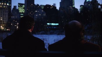 Movie still from “Death to Smoochy” (2002), directed by Danny DeVito – Two men sitting in front of a city skyline at night; Medium shot, Over the shoulder angle