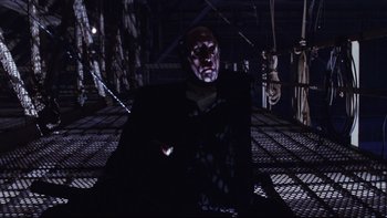 Movie still from “Death to Smoochy” (2002), directed by Danny DeVito – A man with a red mask sitting in a dark room; Medium shot, Low angle