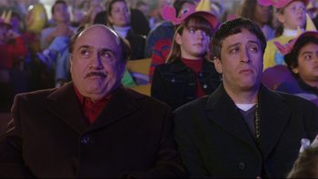 Movie still from “Death to Smoochy” (2002), directed by Danny DeVito – Two men sitting next to each other in a crowd of people; Medium shot, High angle