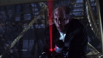Movie still from “Death to Smoochy” (2002), directed by Danny DeVito – A man in a black suit is looking at a red laser beam; Medium shot, Low angle