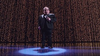 Movie still from “Death to Smoochy” (2002), directed by Danny DeVito – A man standing on a stage holding a microphone; Wide shot, Low angle