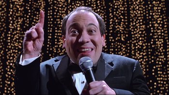 Movie still from “Death to Smoochy” (2002), directed by Danny DeVito – A man holding a microphone in front of lights; Close Up shot, Low angle