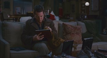 Movie still from “Deck the Halls” (2006), directed by John Whitesell – A man sitting on top of a couch looking at a tablet computer; Medium shot, High angle